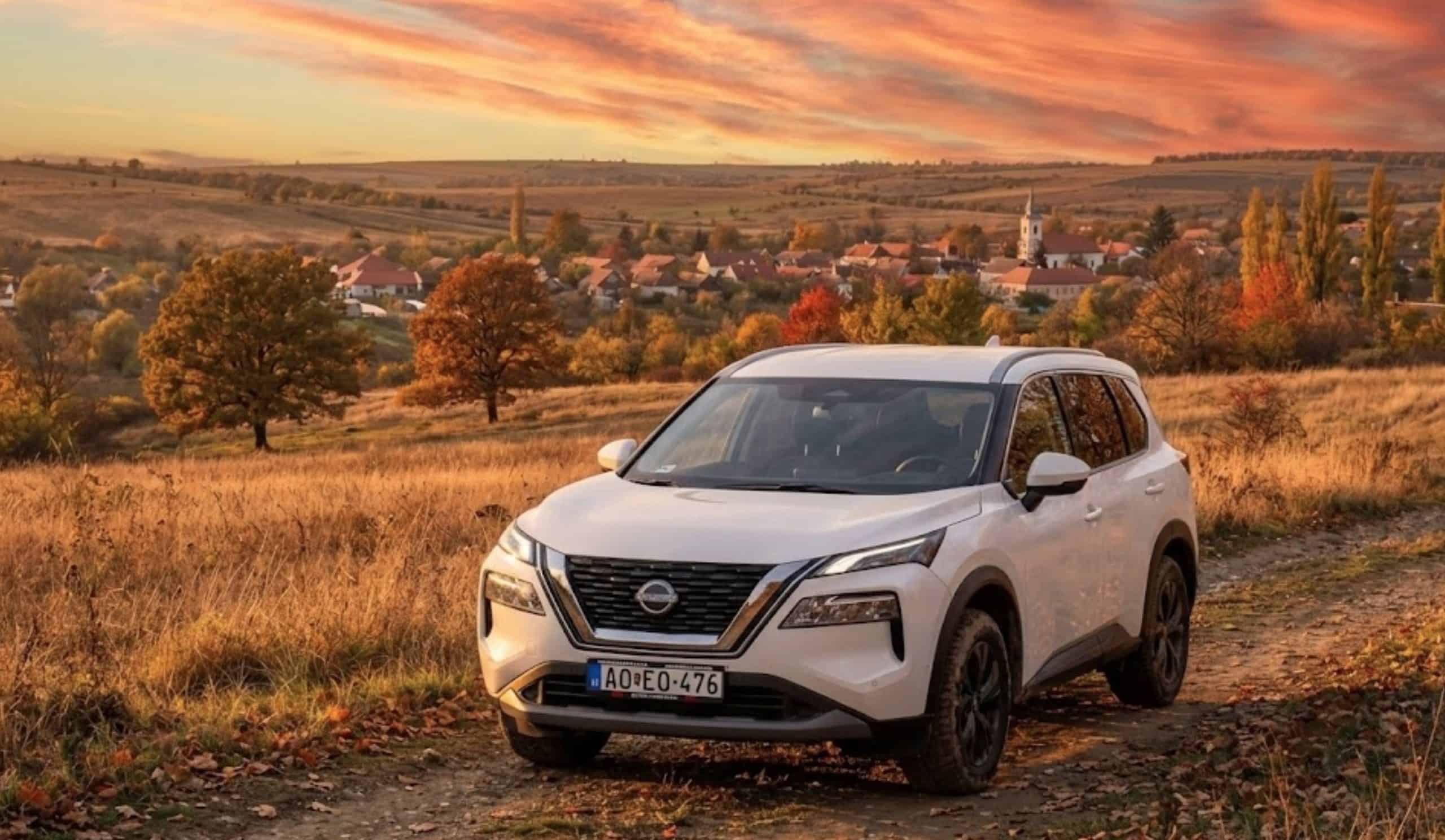 White Nissan X-Trail parked in a scenic autumn countryside at sunset.