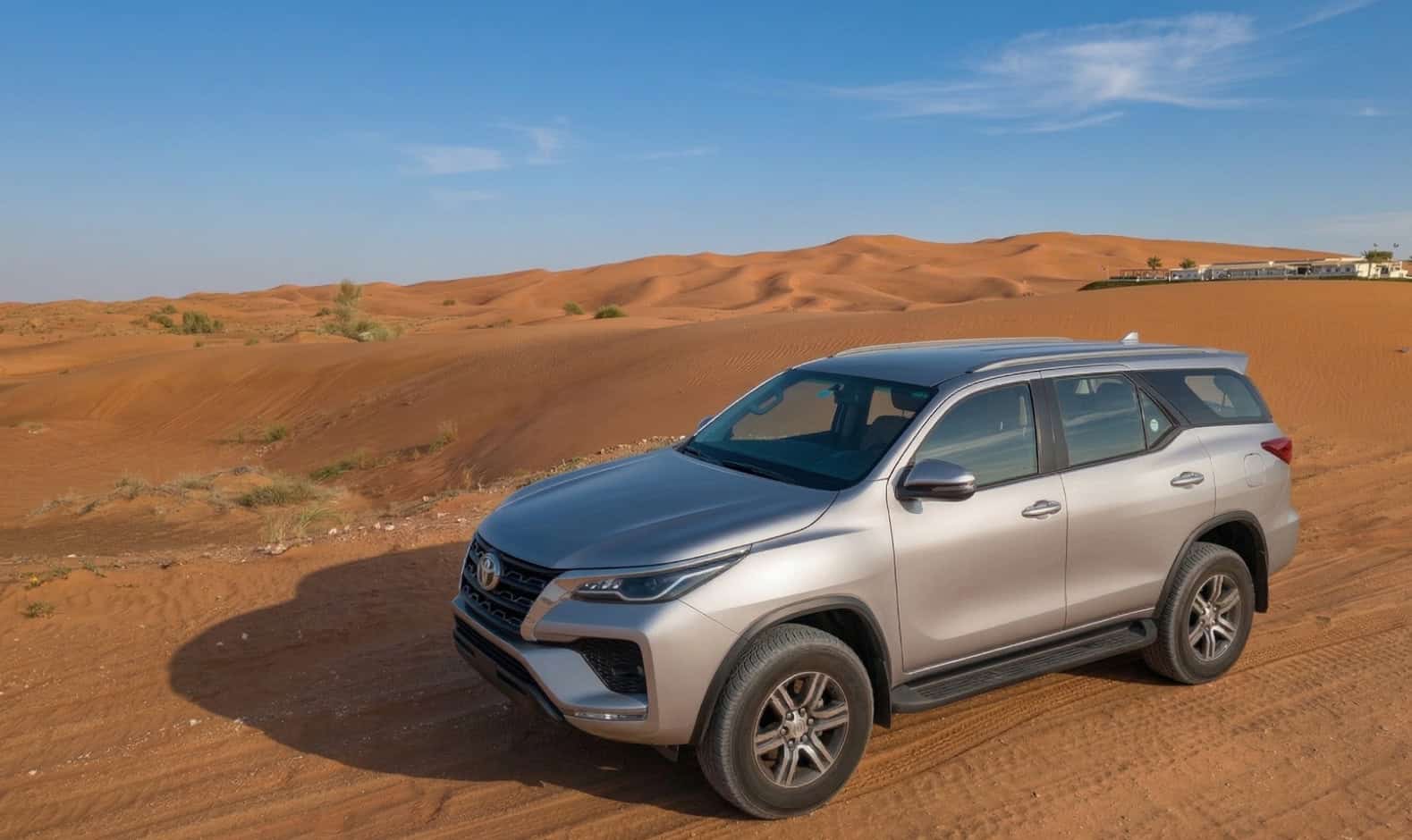 Silver Toyota SUV parked on sandy desert with dunes in background.